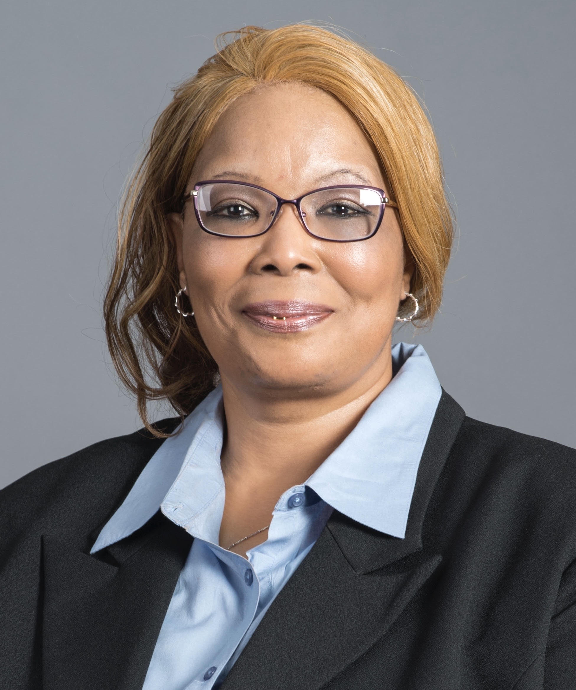Professional woman wearing glasses and a blazer smiles at the camera.